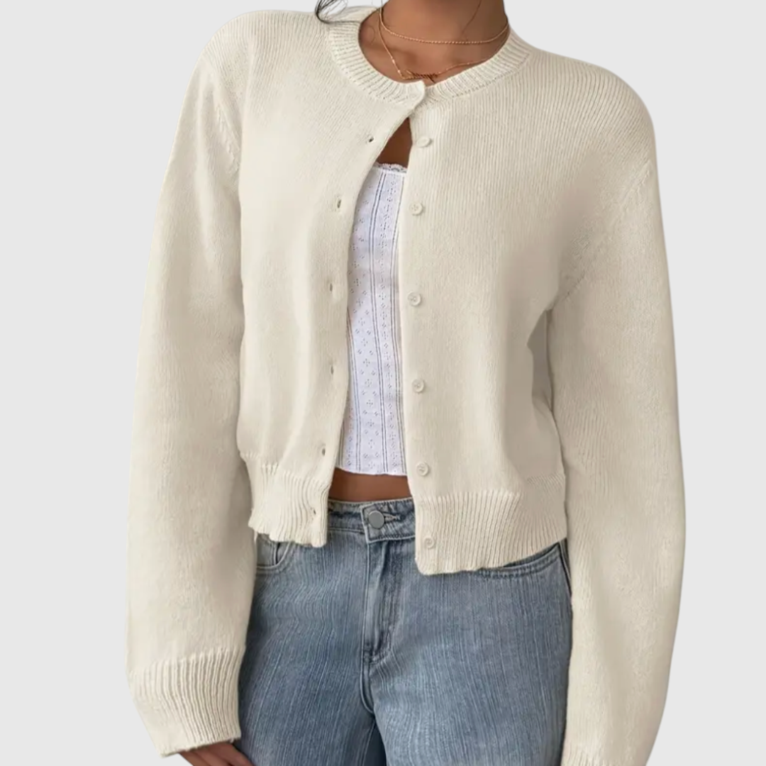 Modell trägt eine kurz geschnittene Strickjacke mit Rundhalsausschnitt und Knopfleiste über einem weißen Top und heller Jeans._0