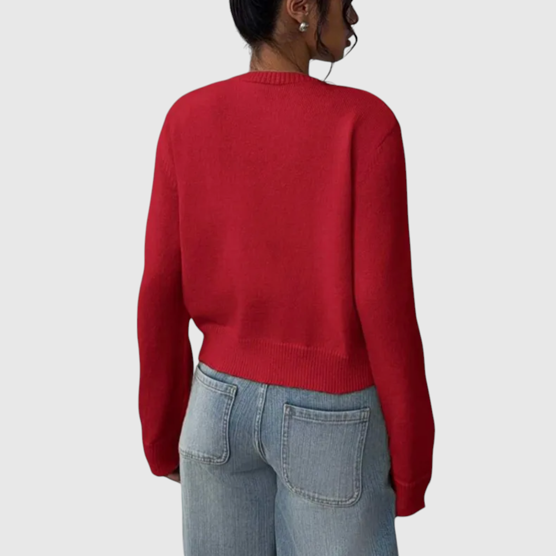 Modell trägt eine kurz geschnittene Strickjacke mit Rundhalsausschnitt und Knopfleiste über einem weißen Top und heller Jeans._13
