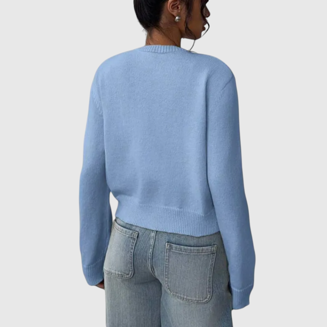 Modell trägt eine kurz geschnittene Strickjacke mit Rundhalsausschnitt und Knopfleiste über einem weißen Top und heller Jeans._15