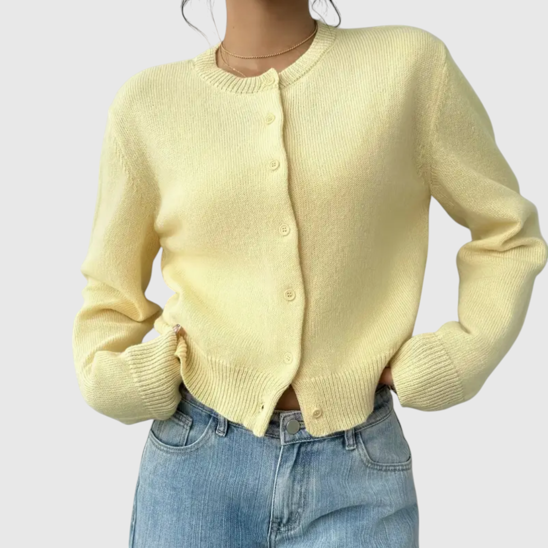 Modell trägt eine kurz geschnittene Strickjacke mit Rundhalsausschnitt und Knopfleiste über einem weißen Top und heller Jeans._17