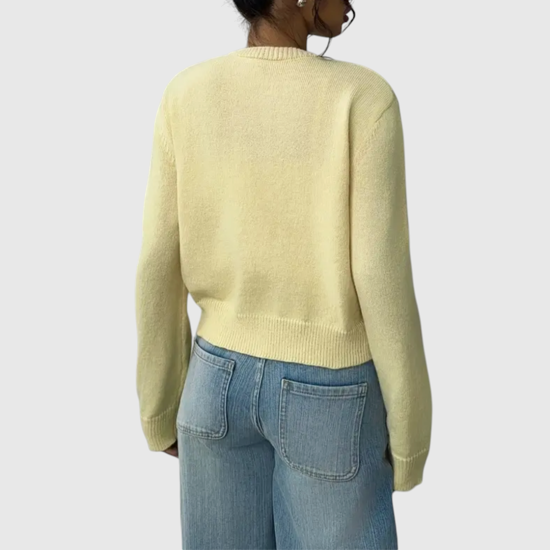 Modell trägt eine kurz geschnittene Strickjacke mit Rundhalsausschnitt und Knopfleiste über einem weißen Top und heller Jeans._18