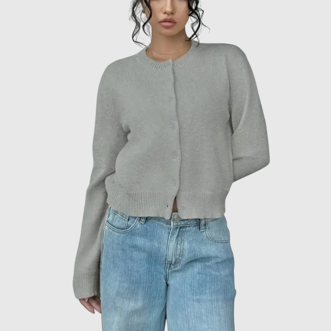 Modell trägt eine kurz geschnittene Strickjacke mit Rundhalsausschnitt und Knopfleiste über einem weißen Top und heller Jeans._6