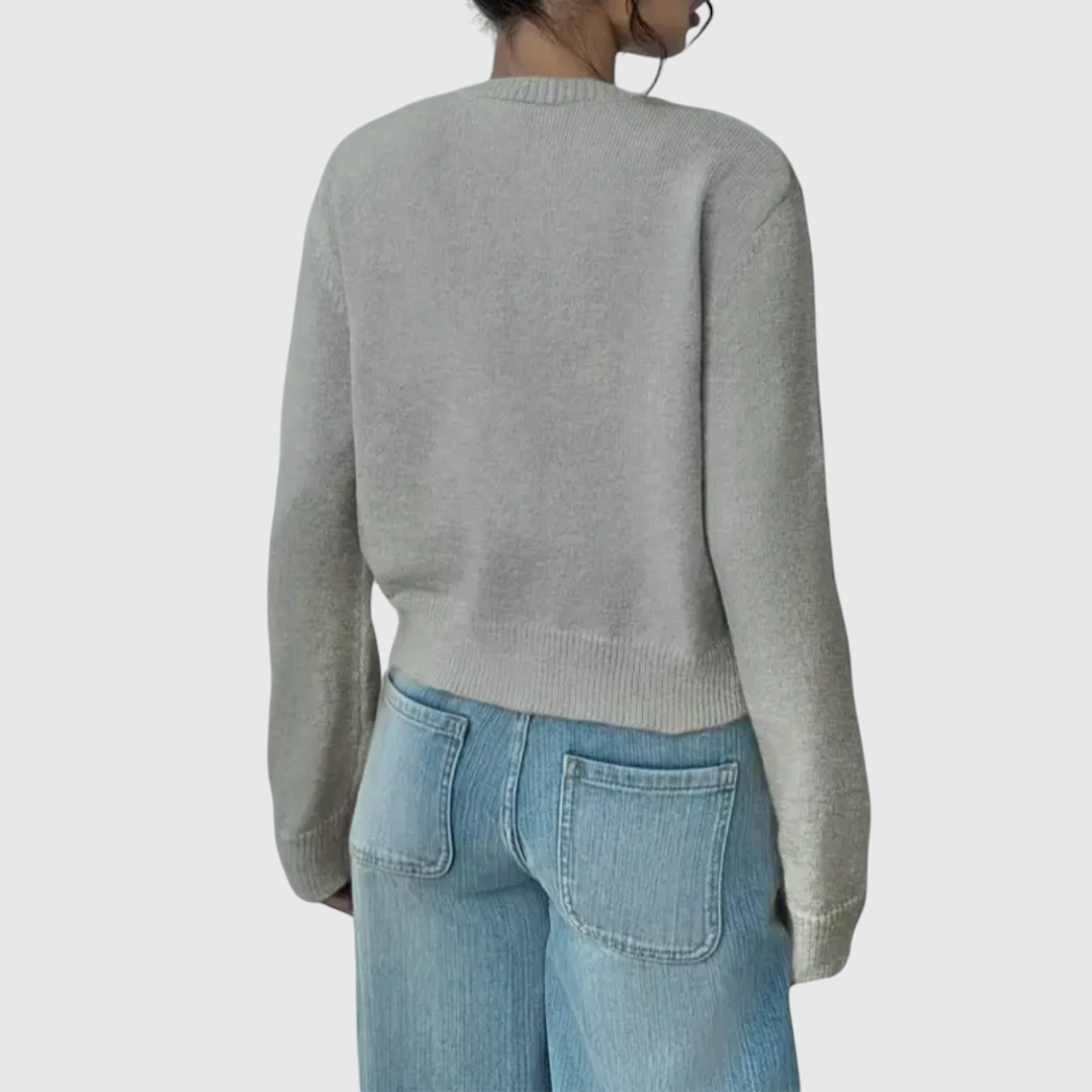 Modell trägt eine kurz geschnittene Strickjacke mit Rundhalsausschnitt und Knopfleiste über einem weißen Top und heller Jeans._7